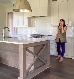 a woman is talking on her cell phone in the kitchen while standing next to an island