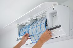 a person working on an air conditioner in a room with white walls and ceiling