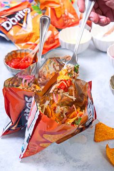 a person scooping food out of a bag with spoons and chips on the table