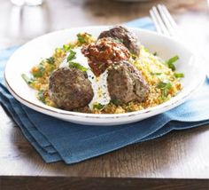 a white plate topped with meatballs and rice on top of a blue napkin next to a fork