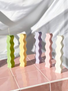 three candles sitting on top of a pink tile floor next to each other in different colors