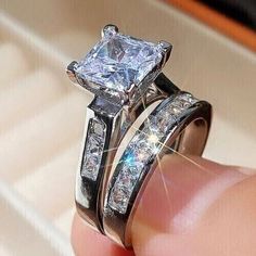 someone is holding their wedding ring with the diamond set on it's finger in front of them