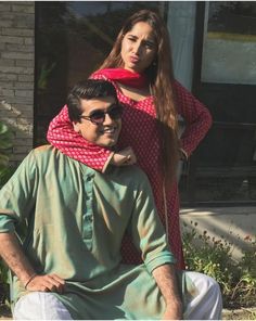 a man sitting next to a woman in front of a building with a red scarf on her head