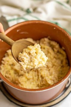 a wooden spoon is being used to scoop mashed potatoes out of a brown pot