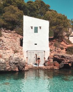 a white building sitting on top of a rocky cliff next to the ocean with blue water