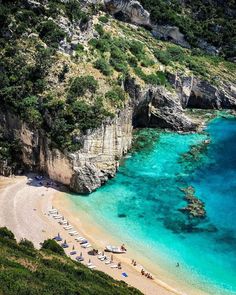 an aerial view of a beach with blue water and umbrellas on the sand, surrounded by cliffs