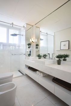 a white bathroom with two sinks and a large mirror above the sink, along with potted plants