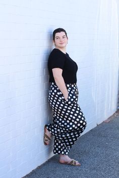 a woman leaning against a white wall wearing polka dot print pants and black top with her hands on her hips