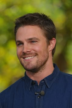 a man with a goatee smiles at the camera while standing in front of trees