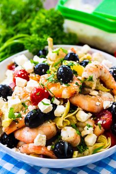 a white bowl filled with shrimp and olives on top of a blue checkered table cloth