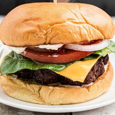 a cheeseburger with meat, lettuce and tomato on a white plate