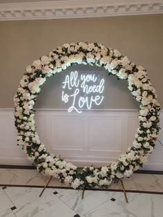 a white flower wreath with the words all you need is love written in neon lights