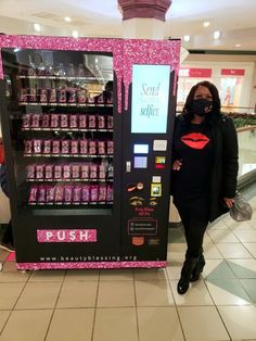 a woman standing next to a vending machine in a shopping mall wearing a face mask