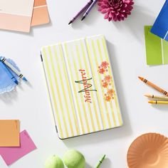 an open notebook sitting on top of a white table next to some pens and paper