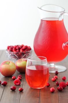 two glasses filled with red liquid next to some cranberries and pomegranates