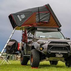 an off road vehicle with a tent attached to it's roof in the grass