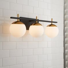 three lights are hanging on the wall above a sink in a white tiled bathroom with black and gold fixtures