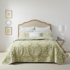 a bedroom with a bed covered in green and white bedspread, two nightstands and pictures on the wall