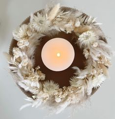 a candle is lit in the center of a wreath made with feathers and flowers on a white background