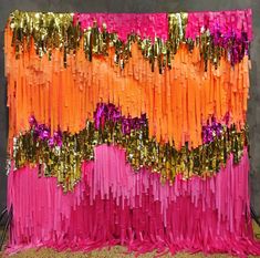 an orange, pink and gold streamer backdrop on a metal stand in front of a gray wall