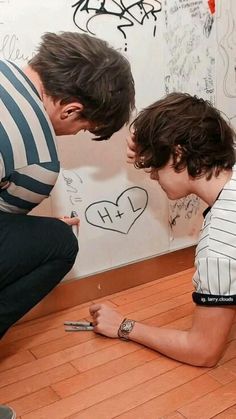 two young men writing on a whiteboard in front of a wall covered with graffiti