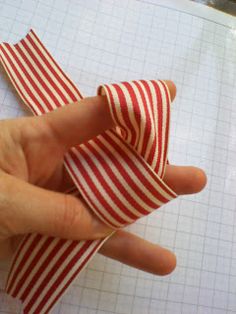 someone is holding two pieces of red and white striped fabric in their hand while they are sewing