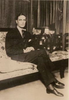 an old black and white photo of a man in a suit sitting on a couch