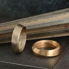 two gold wedding bands sitting next to each other on top of a black surface in front of a window