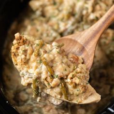 a wooden spoon full of food in a crock pot with meat and vegetable mixture