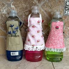 three water bottles with aprons on them sitting next to each other in front of a stone wall