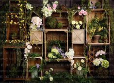 several wooden crates filled with flowers and greenery on top of each other in front of a wall