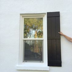 a person standing next to a window with black shutters on the side of it