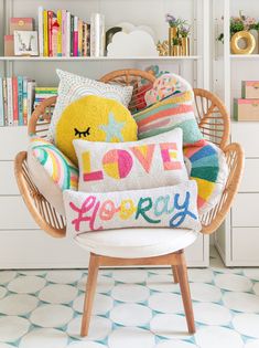 a wicker chair filled with pillows in front of a bookshelf