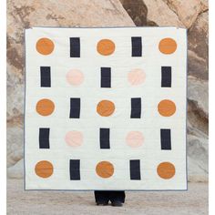 a person holding up a quilt with orange and black circles on it in front of some rocks