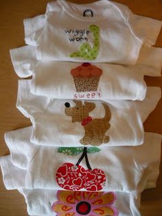 four baby ones with different designs on them sitting next to each other in front of a wooden table