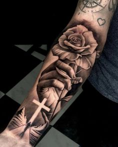 a black and white rose with a cross tattoo on the left arm, in front of a checkered floor