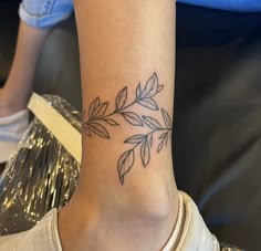 a woman with a tattoo on her ankle that has leaves on it and is wearing a white t - shirt