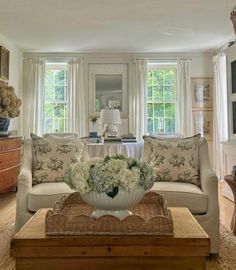 a living room filled with furniture and flowers on top of a coffee table in front of a window