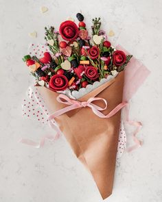 a bouquet of flowers wrapped in brown paper with pink ribbon on a white table top