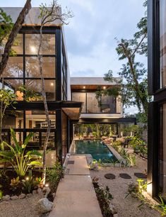 an outdoor area with a pool, trees and plants in front of the house at dusk