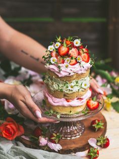 a woman is decorating a cake with strawberries and daisies