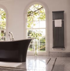 a bathtub sitting in front of two windows next to a white rug on the floor