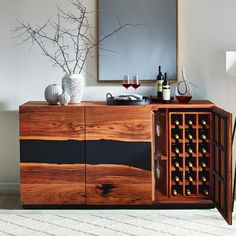 a wooden cabinet with wine glasses and bottles in it next to a mirror on the wall