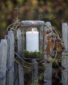 a candle that is sitting on top of a wooden fence with moss and pine cones around it