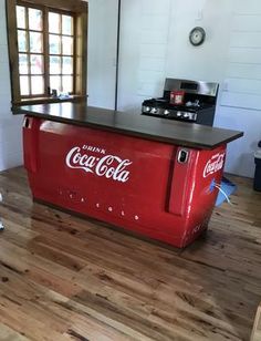 an old coca - cola cooler in the middle of a room with wood flooring