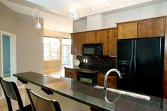 an empty kitchen with black appliances and wooden cabinets, along with bar stools in front of the counter