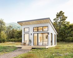 a small white house sitting on top of a lush green field next to a forest