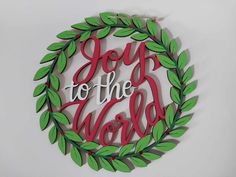 a wooden sign that says joy to the world in red and green leaves around it