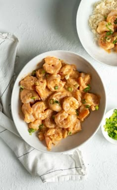 two bowls filled with shrimp and rice on top of a white tablecloth next to a bowl of sauce