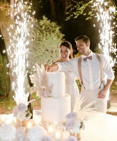 a newly married couple cutting their wedding cake with sparklers in the air behind them